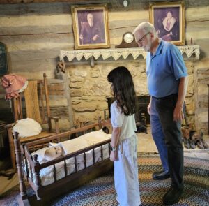 man and his granddaughter looking at crib in a pioneer house
