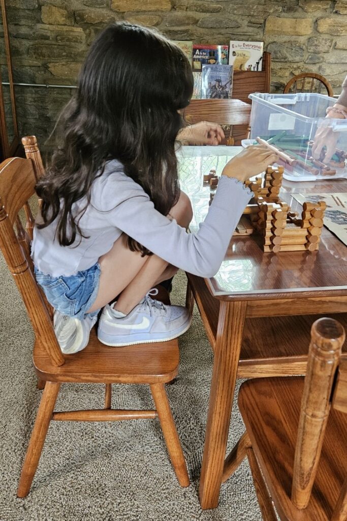 Girl builds a log cabin with Lincoln Logs.