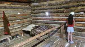 Girl peeks through tiny log cabin window.